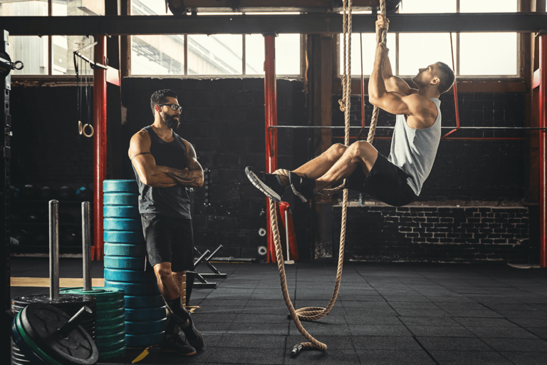 athlete and trainer climbing rope at gym