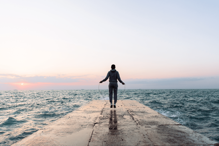 man jumping rope on a lake dock