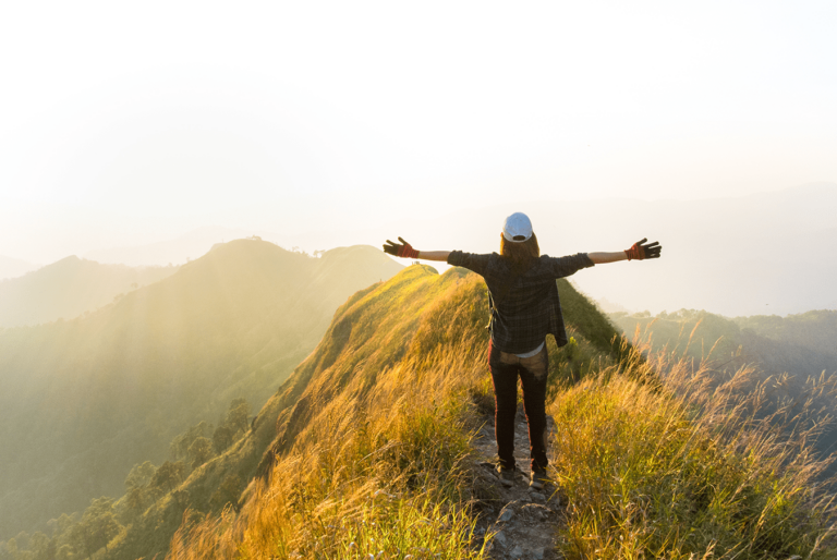 person standing on mountain top with arms outstretched